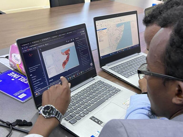 two men sitting in front of two laptops, looking on maps