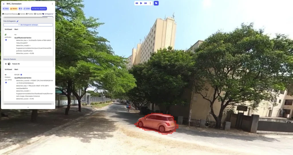 Red SUV parked on a dirt road beside tall trees and a multi-story beige building under a clear sky.