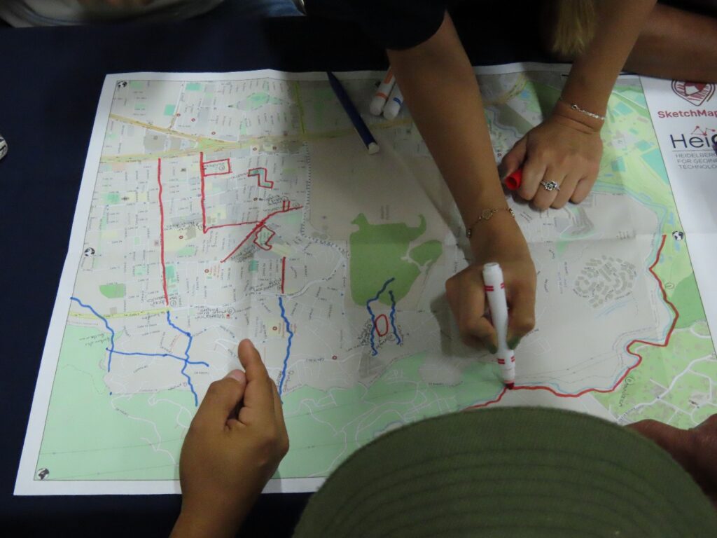 Hands of three people marking routes on a printed map with red and blue markers