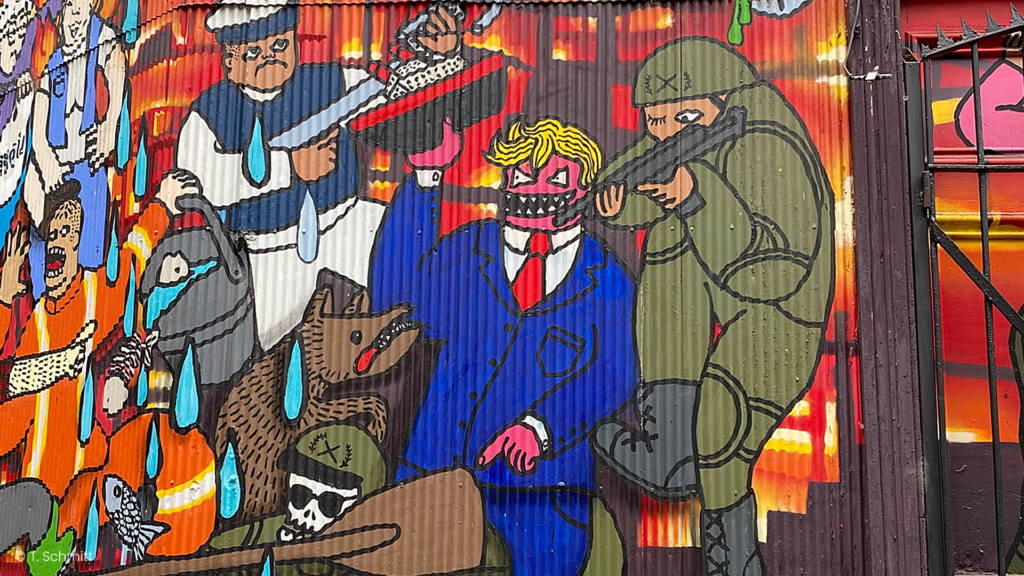 Mural showing a man in a blue suit with a red tie and a mask, a person in a green hazmat suit, a dog, and a police officer holding a baton against a fiery background