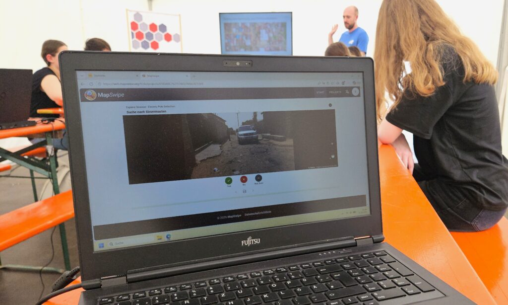 Laptop showing a street view on screen with people sitting and a man standing in the background in a classroom or workshop setting