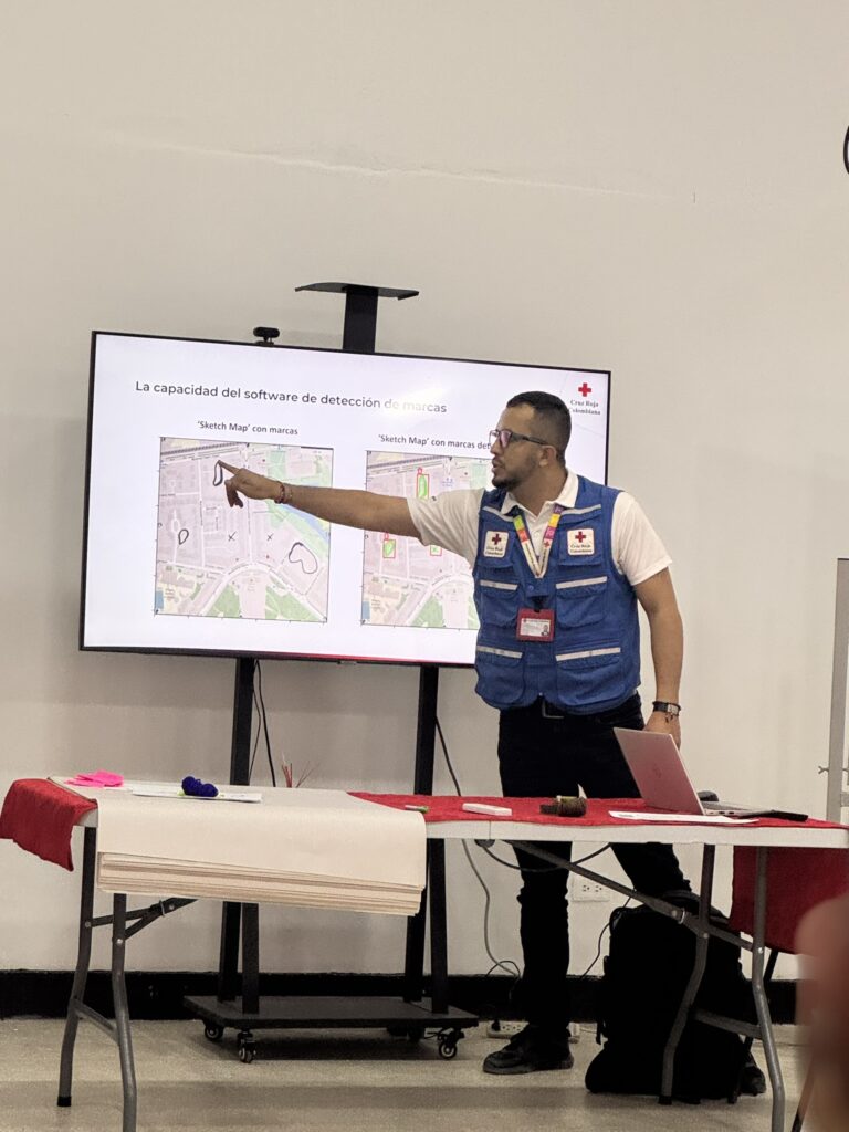 Man in a blue vest pointing at a screen showing maps with Spanish text in a presentation room