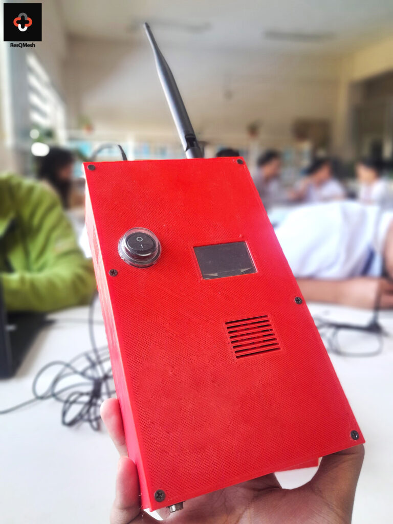 Hand holding a red rectangular electronic device with antenna, switch, small display, and speaker grille